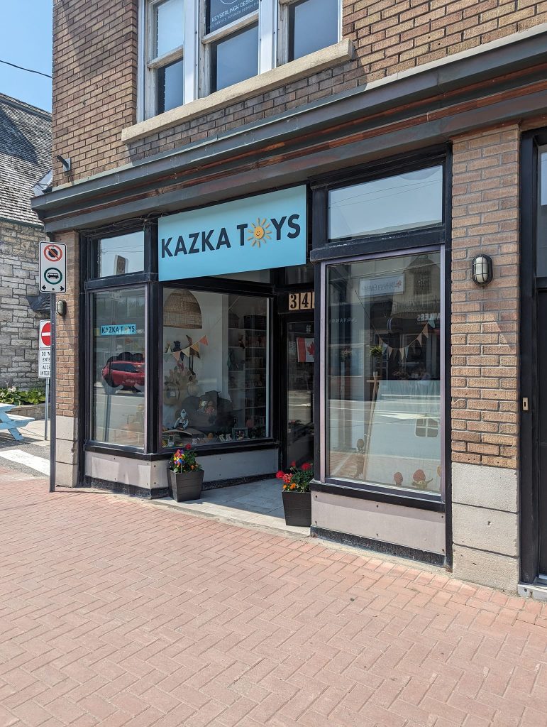 A bright and playful storefront sign for Kazka Toys displayed on a brick building.