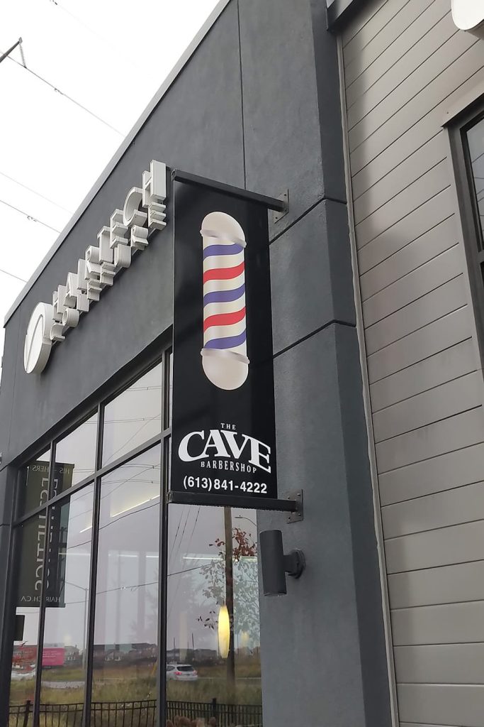 A modern vertical sign for a barber shop featuring a barber pole icon mounted on a building's exterior.